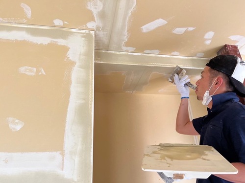 松戸市のアパート室内で職人がパテ処理を行っている様子。塗装前に壁の凹凸を整えて滑らかに仕上げている。